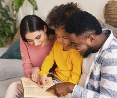 Ebeveynler kızına evde kitap okumasında yardım ediyor.