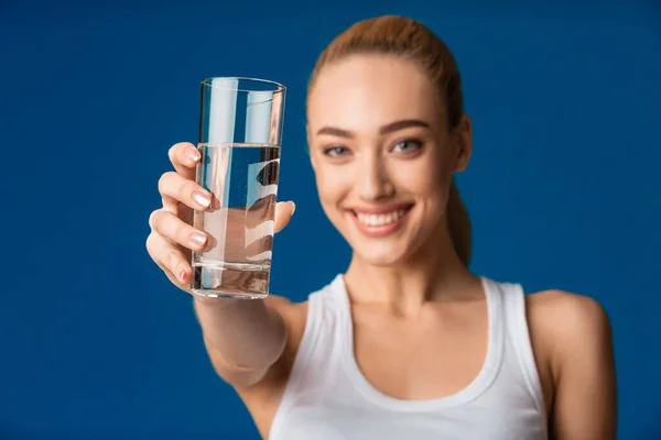 青い背景にカメラに水のガラスを提供する女の子 — ストック写真