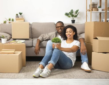 Afro-Amerikalı gülümseyen çift ellerinde kutularla yerde oturuyor.