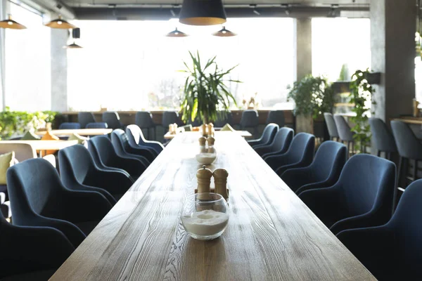 Langer Holztisch mit weichen Stühlen in gemütlichem Café — Stockfoto