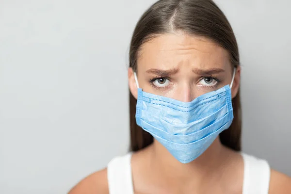 Menina infeliz vestindo máscara durante a pandemia posando sobre fundo branco — Fotografia de Stock