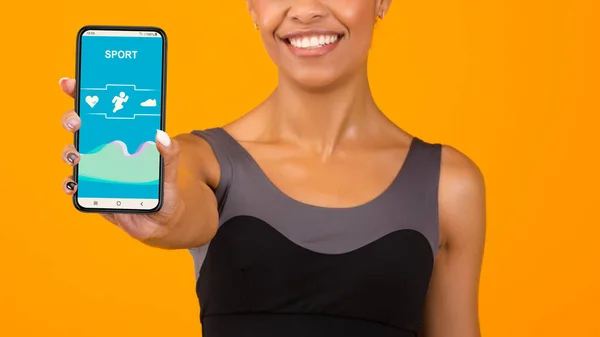 Αθλητική Αφροαμερικανίδα γυναίκα δείχνει κινητό τηλέφωνο με fitness tracker app σε κίτρινο φόντο, closeup — Φωτογραφία Αρχείου
