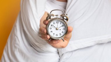 Çalar saati olan battaniyeli bir adam.