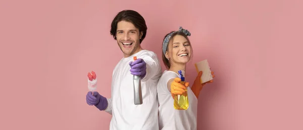 Casal alegre com pulverizadores e ferramentas de limpeza posando sobre fundo rosa — Fotografia de Stock