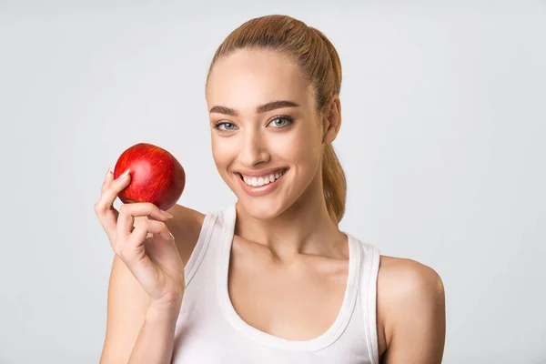 Beyaz dişli kız Kırmızı Elma tutuyor Gülümsüyor, Gri Arkaplan — Stok fotoğraf