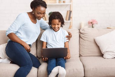 Afro anne ve kızı kanepede dizüstü bilgisayar kullanıyor.