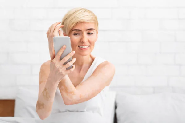 Frau mittleren Alters berührt Haare lächelnd und schaut in Handy — Stockfoto