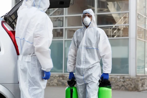 Homem de traje coronavírus segurando frascos de spray com produtos químicos desinfectantes — Fotografia de Stock