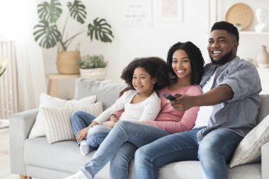Gülümseyen Afro-Amerikan ailesi oturma odasında rahatlıyor ve televizyon seyrediyor.