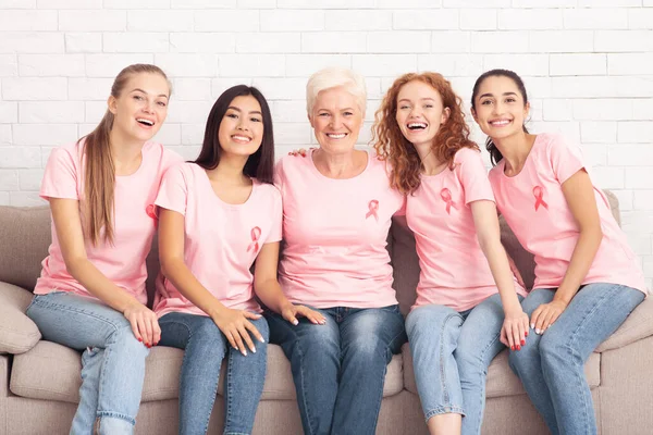 Vidám nők rózsaszín pólóban Mosolyogva ül a kanapén — Stock Fotó