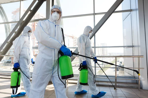 Professionele medewerkers in hazmat pakken desinfecteren overdekte accommodatie — Stockfoto