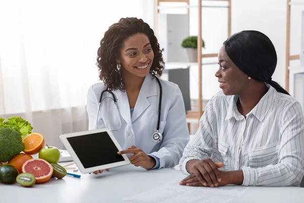 Freundlicher Diätologe zeigt schwarzer Patientin leeren digitalen Tablet-Bildschirm — Stockfoto