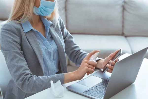 Женщина в медицинской маске дезинфицирует устройства во время работы — стоковое фото