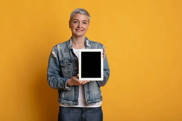 Όμορφη μεσήλικη γυναίκα δείχνει ψηφιακή ταμπλέτα με λευκή μαύρη οθόνη — Φωτογραφία Αρχείου