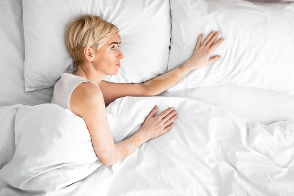 Smutný středního věku žena ležící v manželské posteli sahá pro svého manžela — Stock fotografie