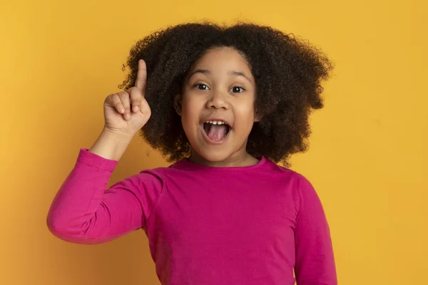想法的概念。一个黑人小女孩用手指在黄色的背景上 — 图库照片