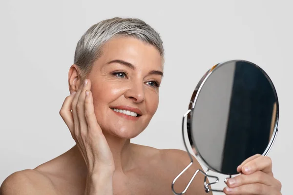 Gyönyörű érett hölgy néz tükör és alkalmazása anti-aging krém — Stock Fotó