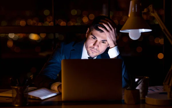 Nachdenklicher Geschäftsmann schaut auf Laptop, der nachts im Büro sitzt — Stockfoto