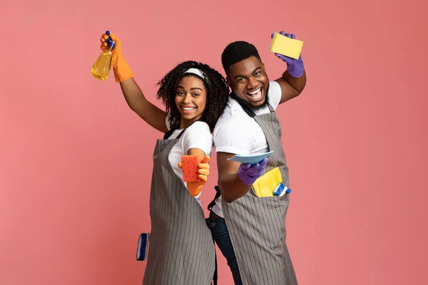 Happy african couple posing with sponges, sprayer and rag, pink background — Stock Photo, Image