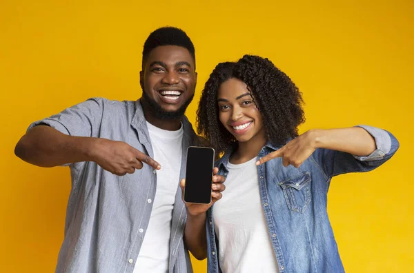 Vrolijk Afrikaans paar wijzen naar smartphone met zwart scherm voor mockup — Stockfoto
