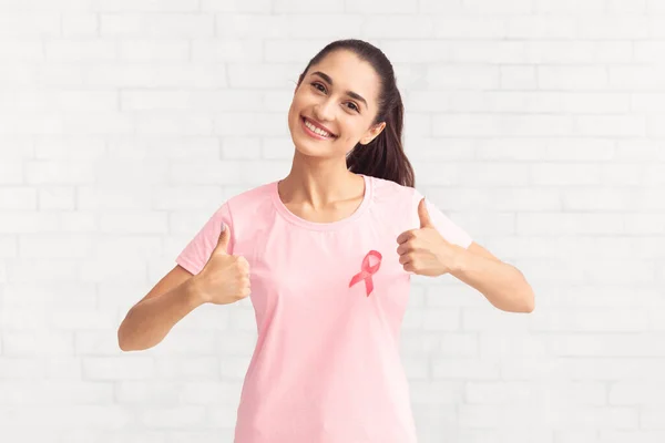 Девушка с розовой раковой лентой Жевательные пальцы вверх на белом фоне — стоковое фото