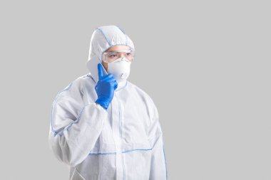 Koruyucu giysili ve eldivenli adam telefonda konuşuyor.