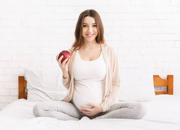 Wanita hamil muda makan apel merah di tempat tidur di rumah — Stok Foto