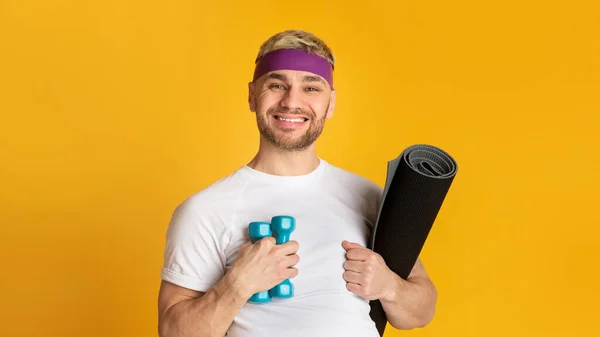 Joven hombre sonriente con mancuerna y colchoneta de fitness — Foto de Stock