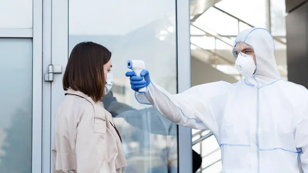 Medisch medewerker in hazmat pak meten temperatuur met contactloze thermometer — Stockfoto