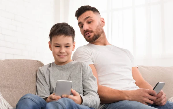 Любопытный отец подглядывает за своим сыном смартфоном дома — стоковое фото