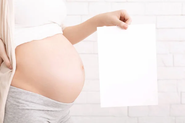 Беременная женщина держит белую карточку возле голого живота — стоковое фото