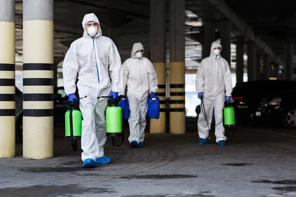 Les hommes en combinaison de protection contre le virus envisagent de désinfecter la ville avec des produits chimiques — Photo