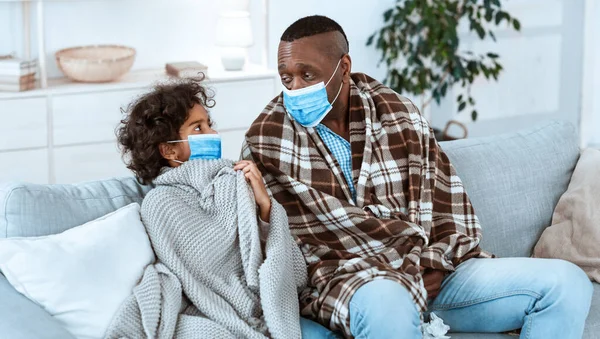 Alerta de salud por Coronavirus. Niña con su abuelo afroamericano usando máscaras protectoras en casa —  Fotos de Stock