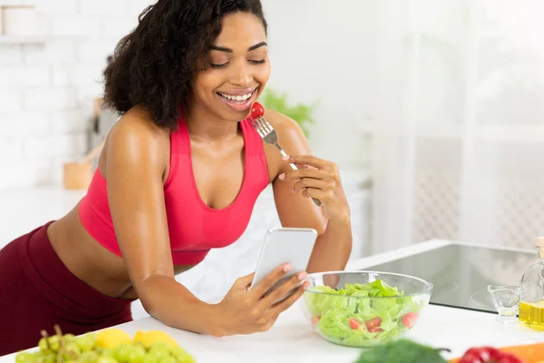 Gadis kulit hitam menggunakan smartphone dan makan salad — Stok Foto