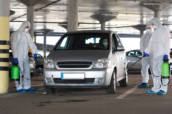 Mężczyźni w kombinezonach antywirusowych dezynfekują samochód chemikaliami — Zdjęcie stockowe