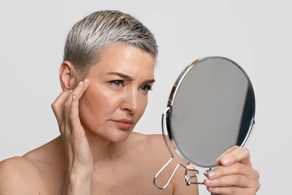 Шкіра старіння. Доросла жінка дивиться у дзеркало, перевіряючи свої зморшки. — стокове фото