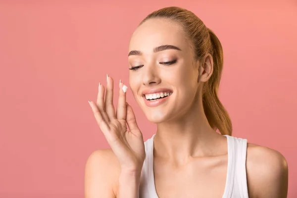 Happy Woman Stosując krem do twarzy na odżywianie skóry, różowe tło — Zdjęcie stockowe