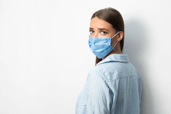Smutná žena na sobě lékařské masky při pohledu na kameru, bílé pozadí — Stock fotografie