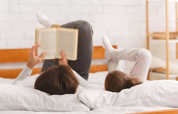 Pai e filhinha deitados na cama, lendo livro — Fotografia de Stock