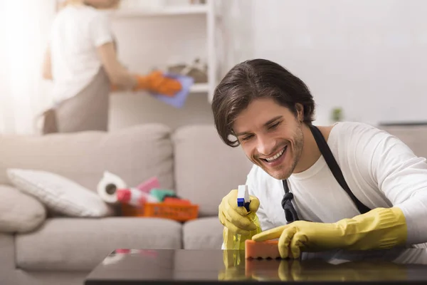 Obligaciones domésticas. Pareja de limpieza de primavera apartamento juntos, hombre limpiando el polvo de la mesa — Foto de Stock