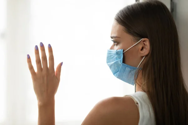 Zieke vrouw in beschermende masker staan in de buurt van venster thuis — Stockfoto