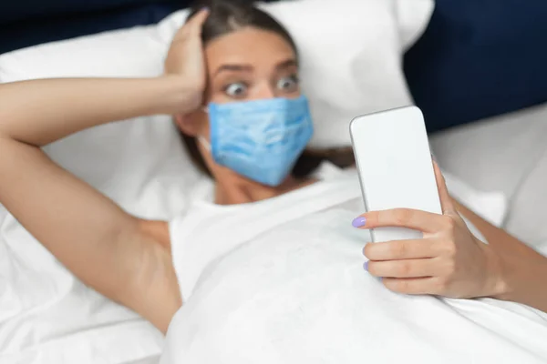 Geschokt meisje in masker lezen Nieuws Online liggen in bed — Stockfoto