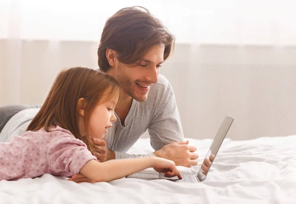 Apa és lánya laptopot használnak, ágyban fekszenek — Stock Fotó