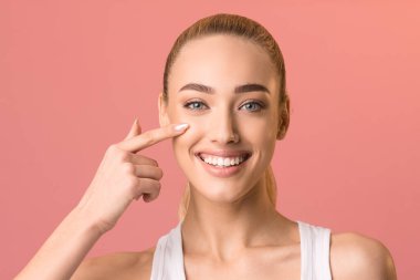 Gülümseyen kız yüz kremi sürerek stüdyoda poz veriyor.