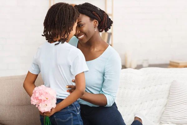 Afro lány gratulál az anyjának virágokkal a kanapén — Stock Fotó