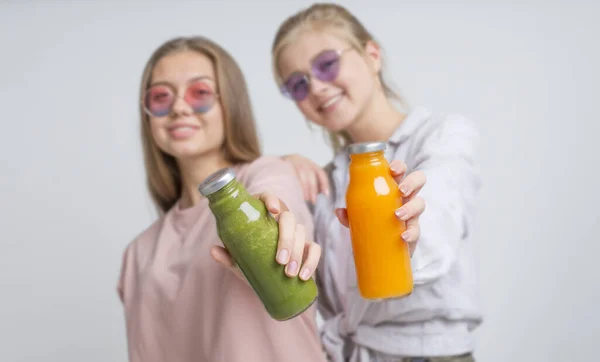 Dos chicas sosteniendo batido de desintoxicación de ingredientes frescos en gris —  Fotos de Stock