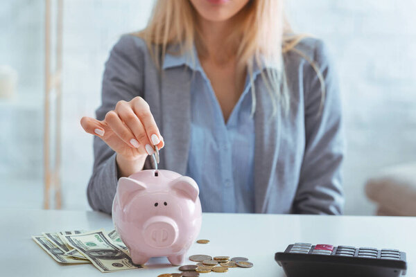 Girl puts coin piggy bank, near cash and calculator