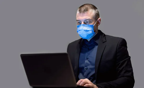 Affärsman i skyddande mask arbetar på laptop över grå bakgrund — Stockfoto