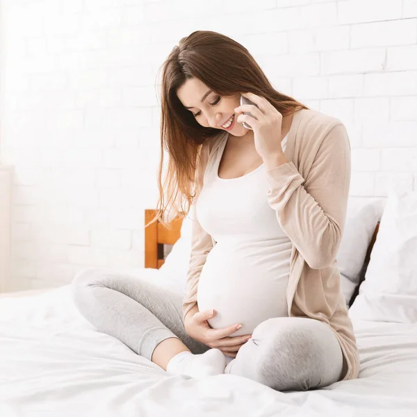 Wanita hamil ceria berbicara di ponsel di rumah — Stok Foto
