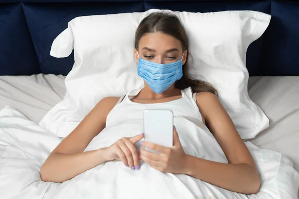 Woman In Medical Mask Texting Lying In Bed At Home — Stock Photo, Image